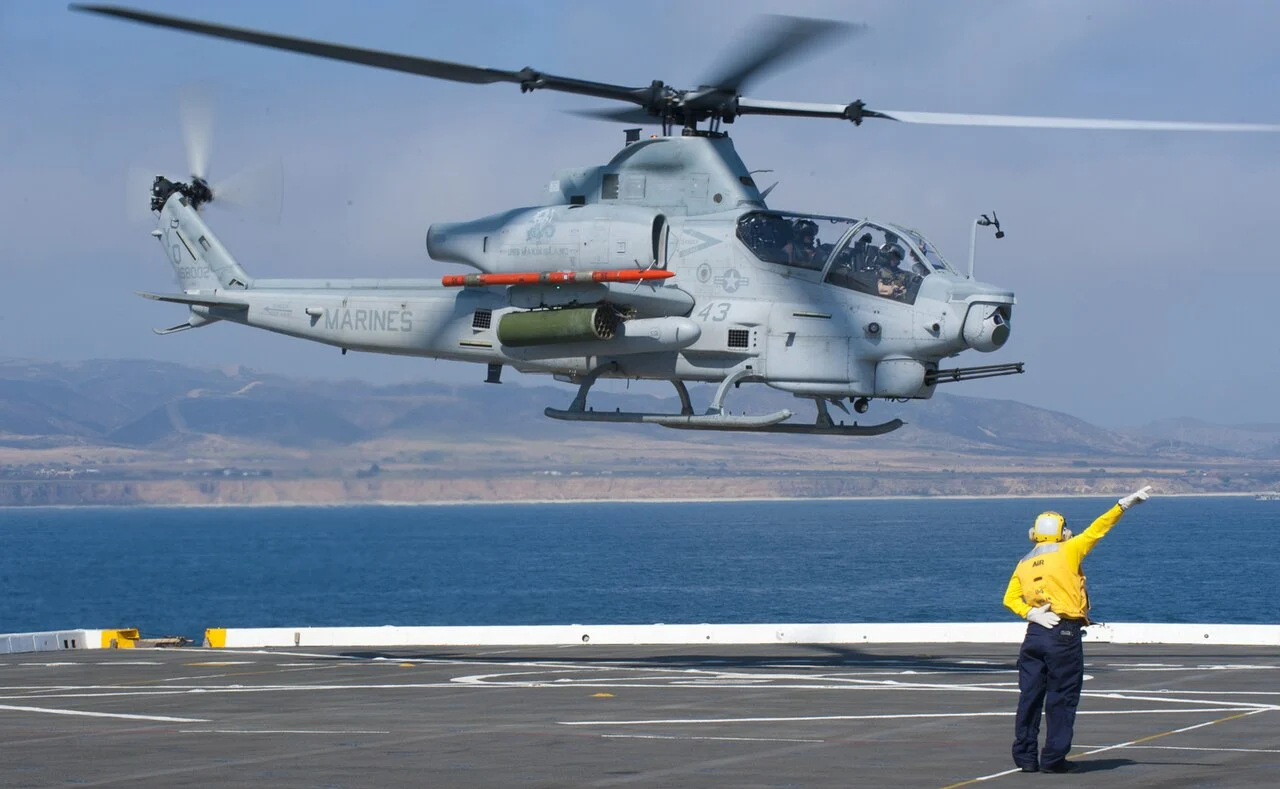 A US Navy sailor guides a Marine Corps AH-1Z Viper attack helicopter on a ship's flight deck